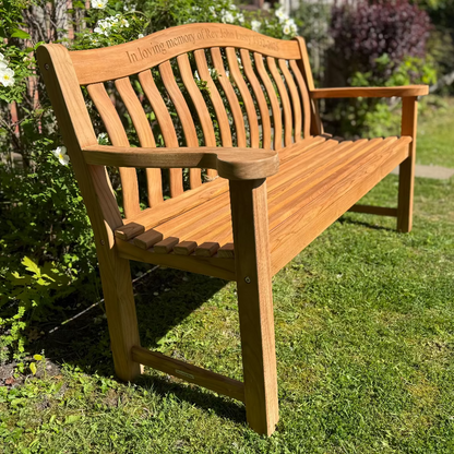 Turnberry Teak memorial bench in a garden setting with greenery and flowers.